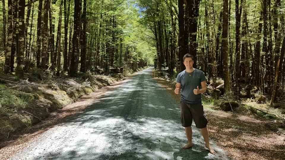 Jonathan standing barefoot on a quiet forest road with sunlight through the trees.